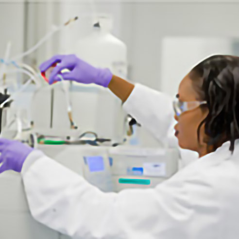 Eine Mitarbeiterin in Schutzkleidung arbeitet an einem analytischen Gerät in einem Labor von Amgen. Symbolbild für Kontaktinformationen der Abteilung für Arzneimittelsicherheit.