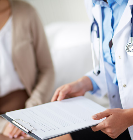 Ärztin im weißen Kittel mit Klemmbrett spricht mit Patientin, Fokus auf medizinische Beratung und Aufklärungsgespräch.