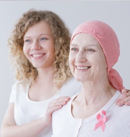 Krebspatientin mit ihrer Tochter. Die Tochter hat die Hände auf die Schultern der Mutter gelegt. Die Mutter trägt die rosa Schleife als Symbol für Brustkrebs.